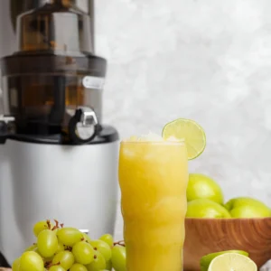 this image show a glass full of green grapes juice that is garnish with grapes with a blender in a background